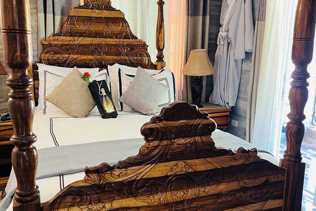 Una cama de madera con intrincados grabados, una lámpara de noche y una bata colgada en la pared.