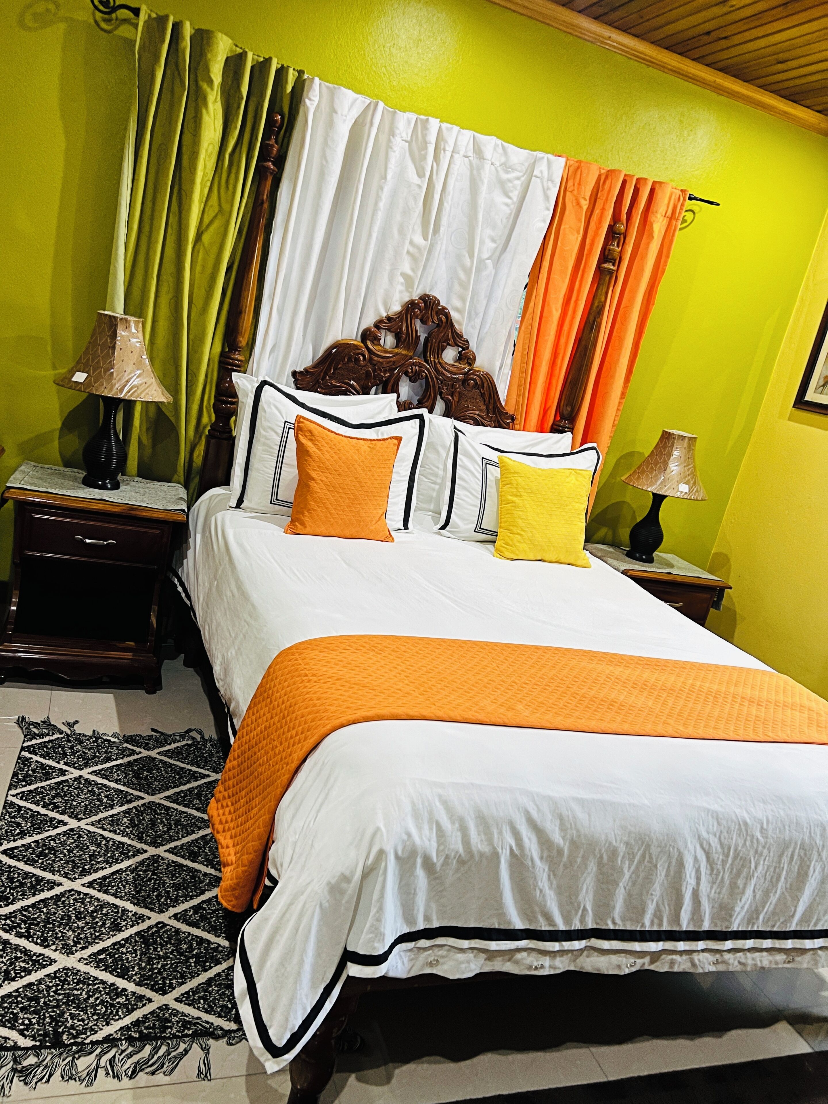 A bed with an orange and white bedspread, two nightstands with lamps, a wooden headboard, and a patterned rug.