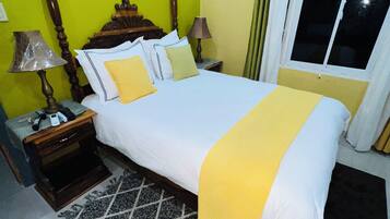 A bedroom with a bed, nightstands, a lamp, a window with curtains, and a wall with a picture.