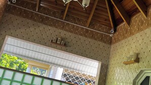 Een kamer met een houten plafond, een kroonluchter, een raam met groene glaspanelen en een betegelde muur.
