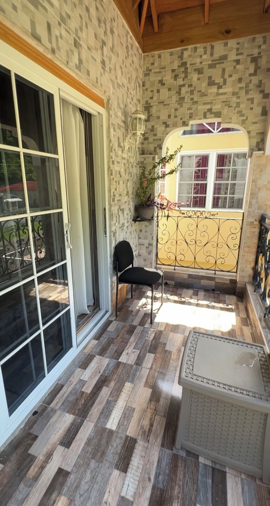 A covered patio with a checkered floor, a black chair, a small table, and a yellow bus-shaped window.