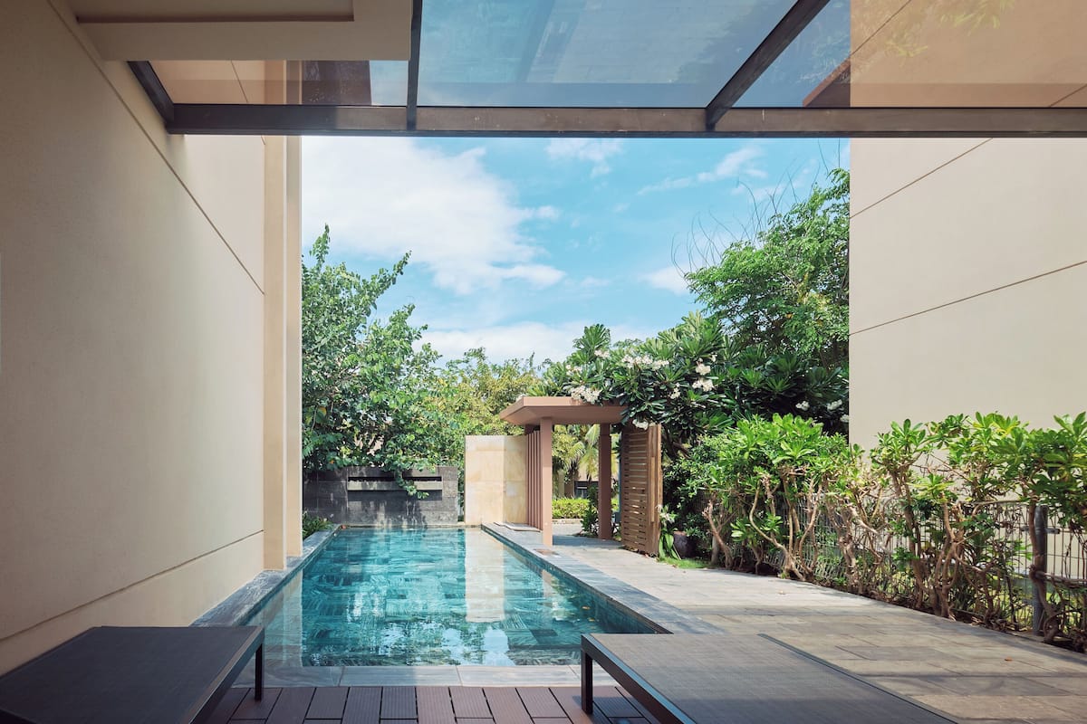 Ein Swimmingpool mit Pergola, umgeben von Grünpflanzen und blauem Himmel.