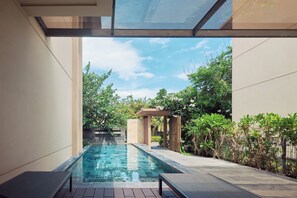 A swimming pool with a pergola, surrounded by greenery and a clear sky.