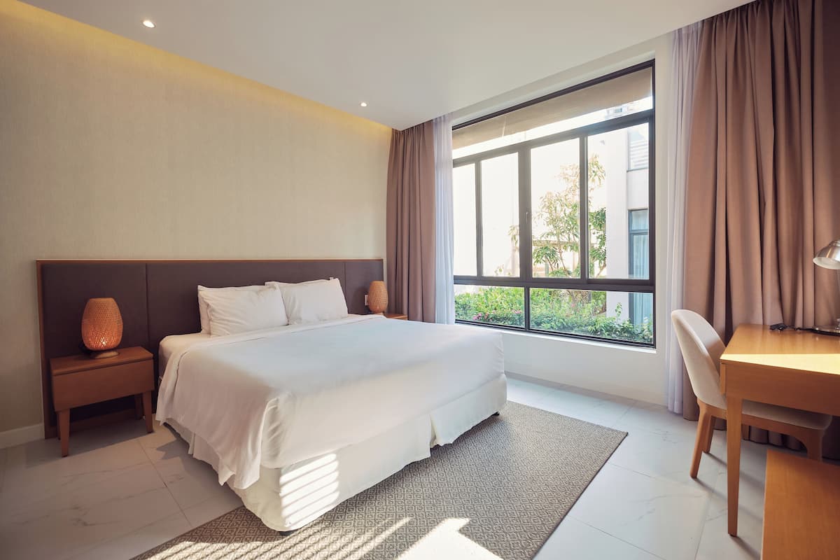 Ein modernes Hotelzimmer mit einem großen Bett, einem Schreibtisch und Blick auf Grünflächen.