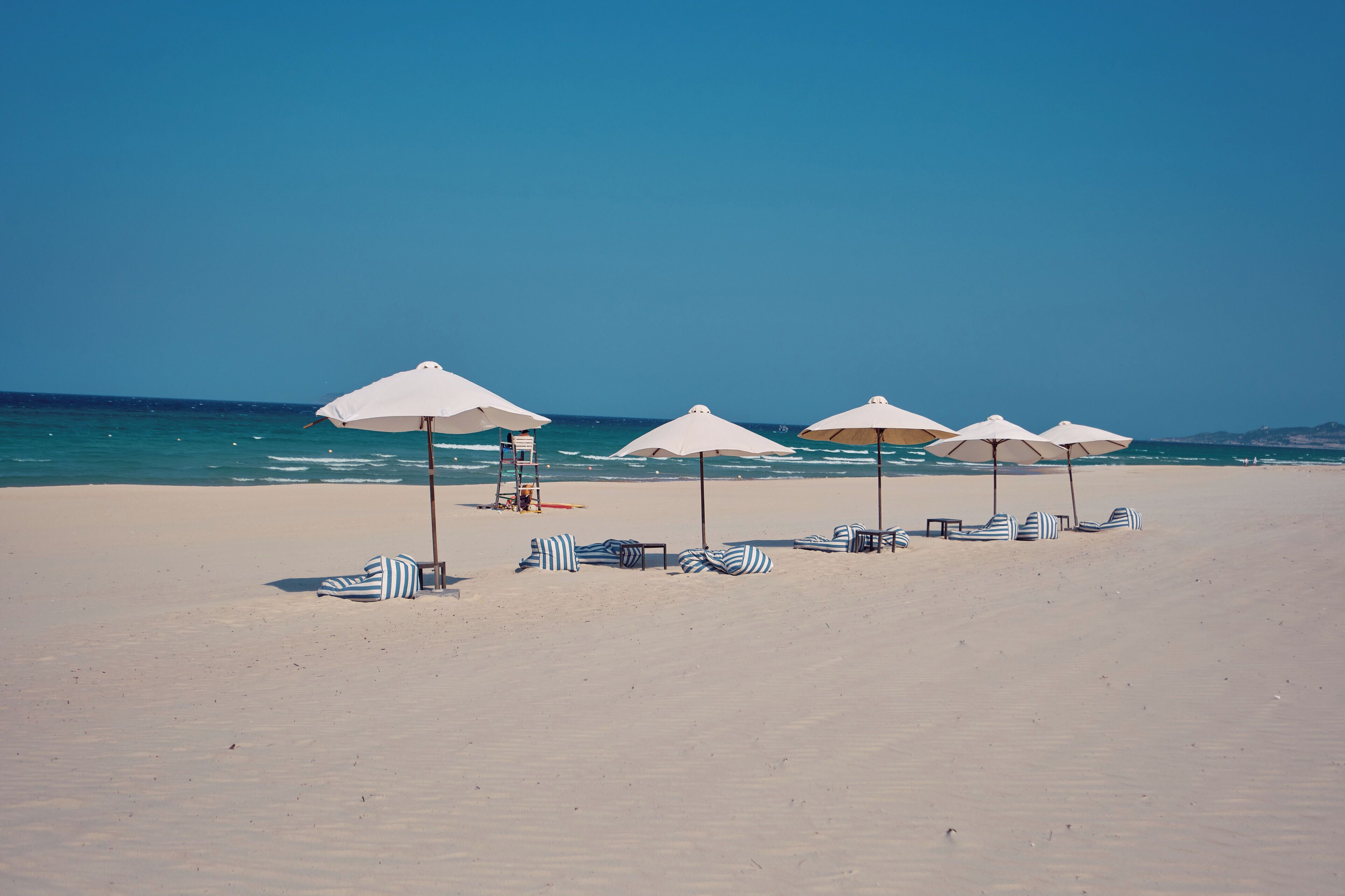 A beach with white umbrellas and striped lounge chairs.