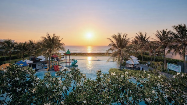 Ein Hotelpool mit Blick auf einen Sonnenuntergang, Palmen und einem Rettungsschwimmerstand.