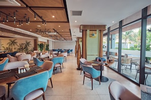 A modern restaurant with high ceilings, wooden paneling, and large windows offering a view of the outdoors.