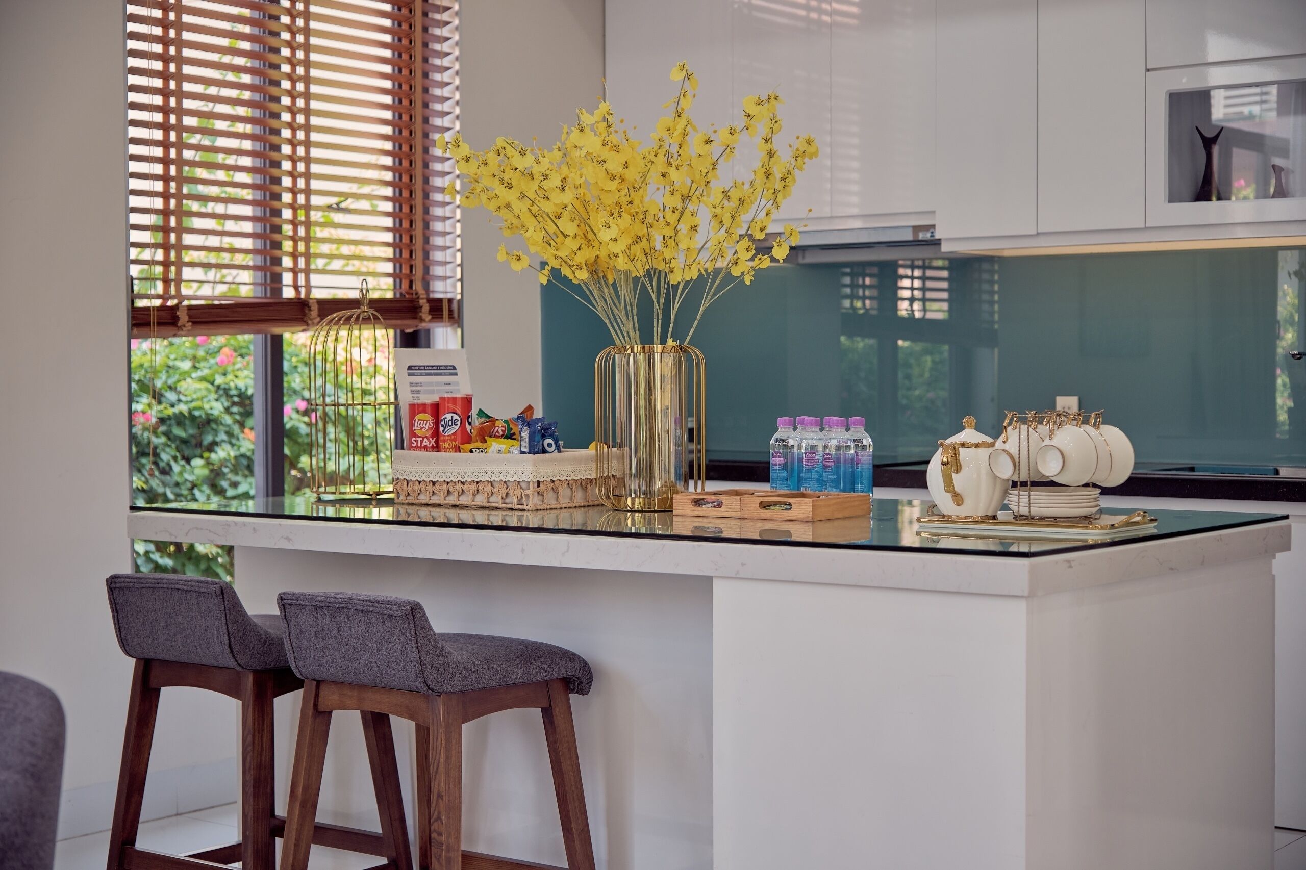 A kitchen island with a vase of yellow flowers, bar stools, and kitchen appliances.