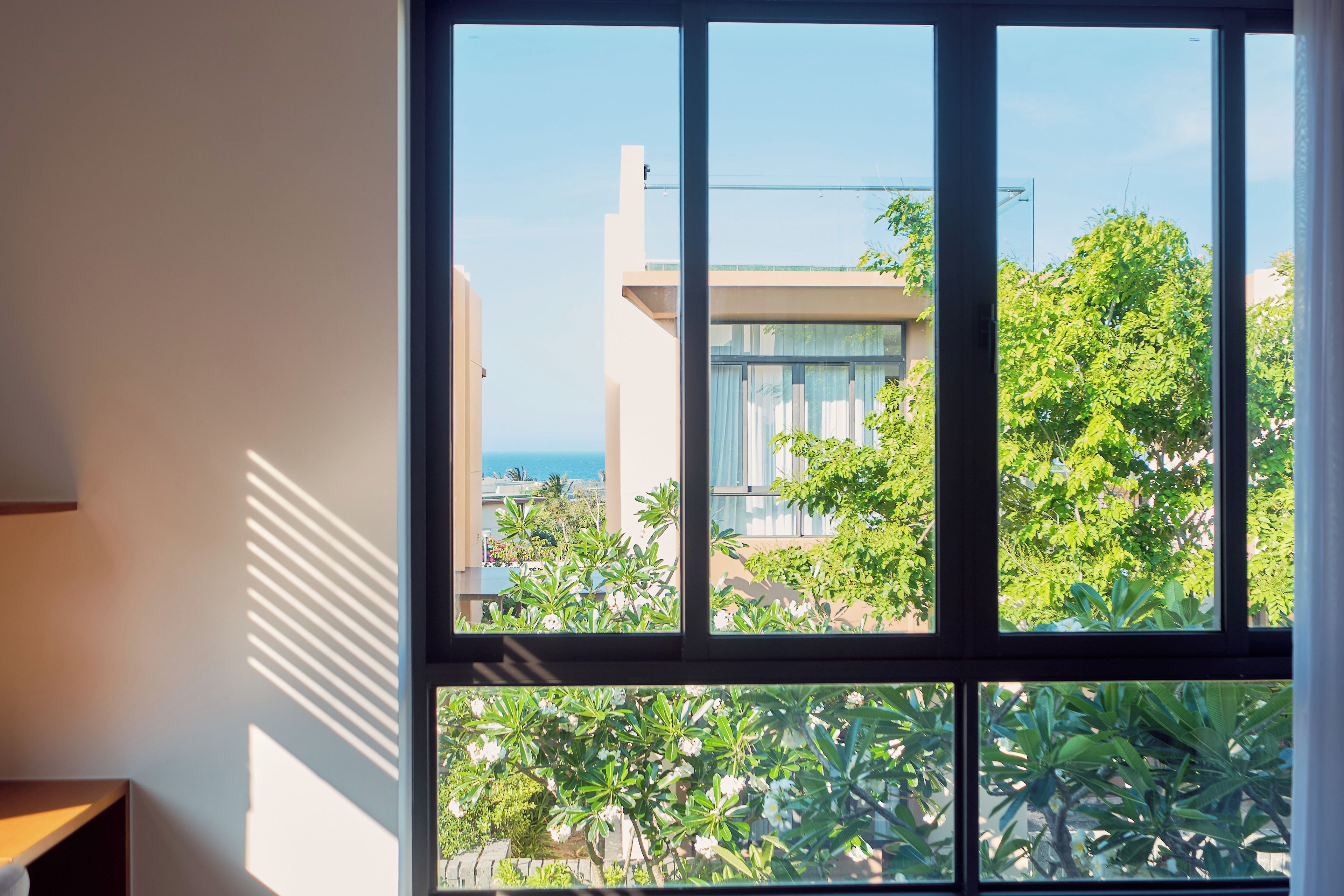 Quarto com uma janela grande, vista de um edifício e vegetação lá fora.