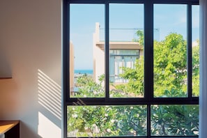 Una stanza con un'ampia finestra, vista su un edificio e presenza di vegetazione all'esterno.