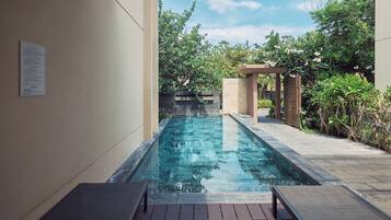 A swimming pool with a wooden deck, surrounded by greenery and a pergola.