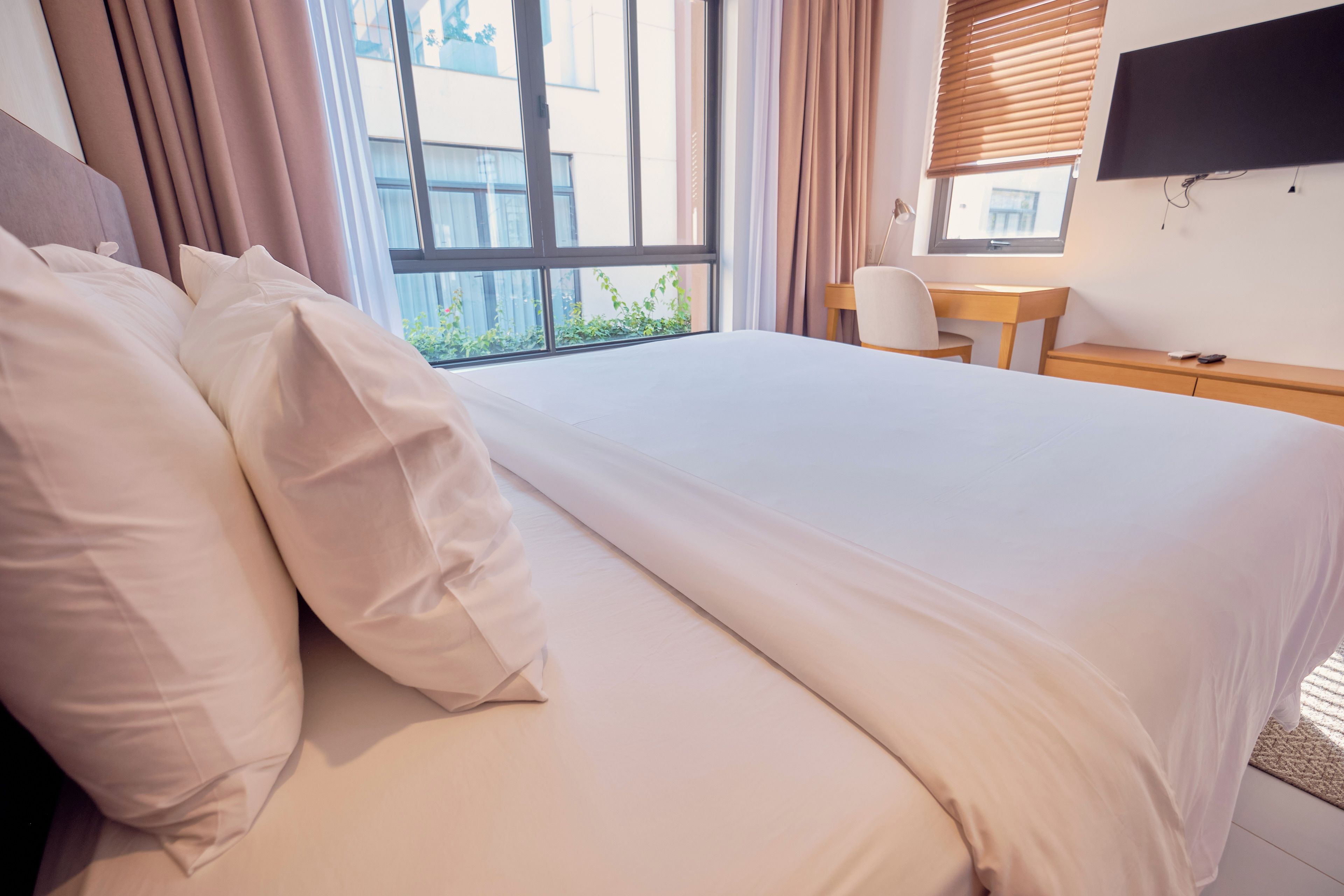 A hotel room with a bed, a desk, and a window with curtains.