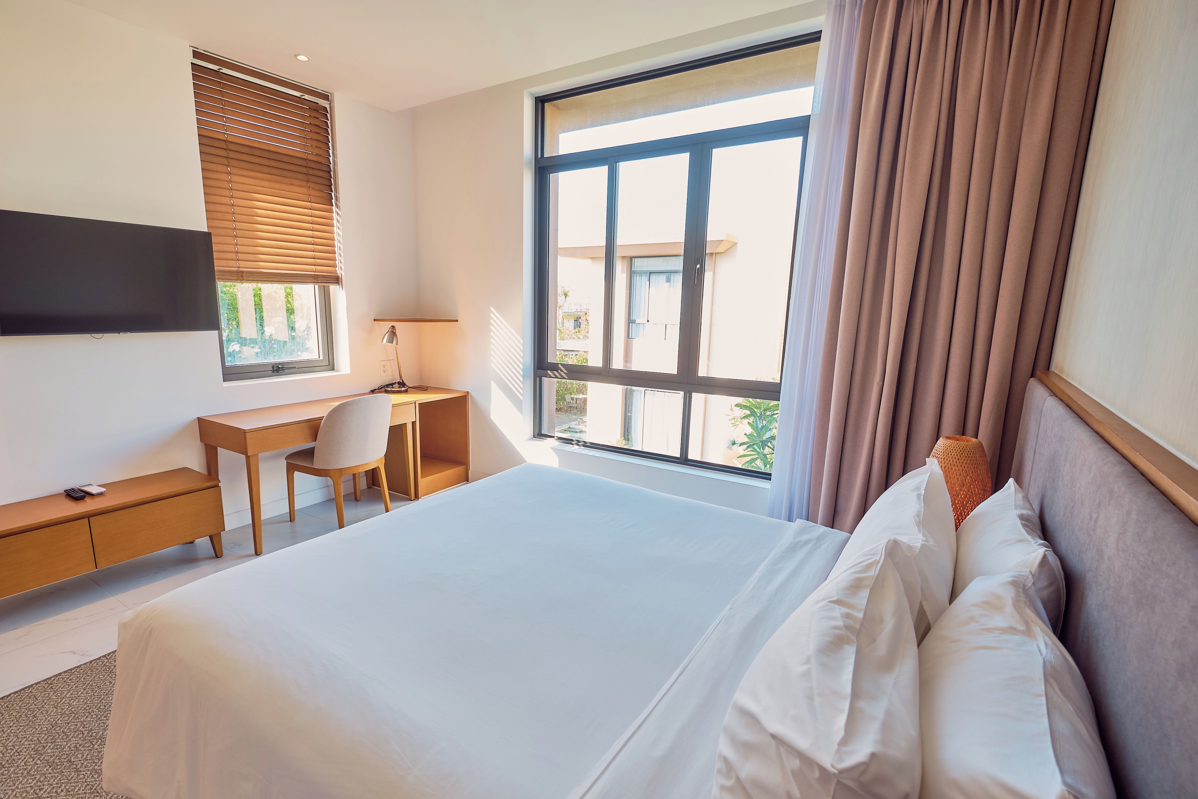 A hotel room with a large bed, a desk, a chair, a TV, and a window with curtains.