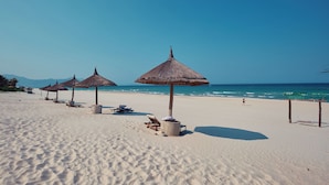 Ein Strand mit Reetdachschirmen, Liegestühlen und freiem Blick auf das Meer.