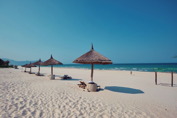 A beach with thatched umbrellas, lounge chairs, and a clear view of the ocean.