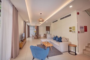 A modern living room with a sofa, coffee table, TV, and dining area. - Sunrise Pool Villa Cam Ranh  (Cam Lam)
