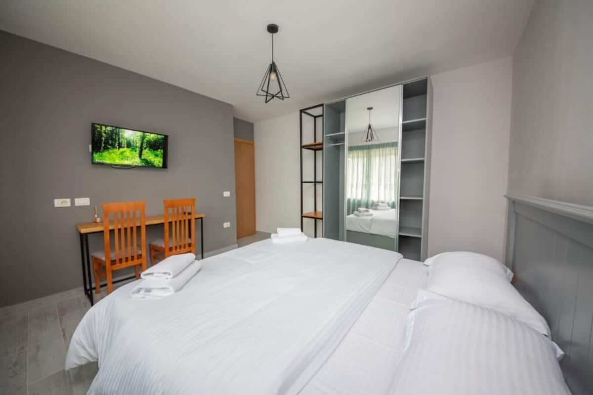 Una habitació d'hotel moderna amb un llit gran, un escriptori amb cadires, una televisió i un armari.