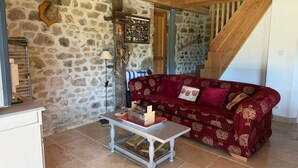 A rustic interior with a stone wall, a wooden ceiling, a red patterned sofa, a small table, and a staircase.
