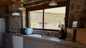 A kitchen with a stone wall, a window, a microwave, a coffee maker, and a toaster.