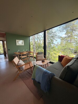 A modern living room with a large window, a sofa, a dining table, and a chair.