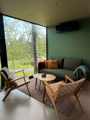 A modern living room with a sofa, two chairs, a small table, and a large window offering a view of trees and sky. - Unique, modern cabin at Blefjell (Svene)