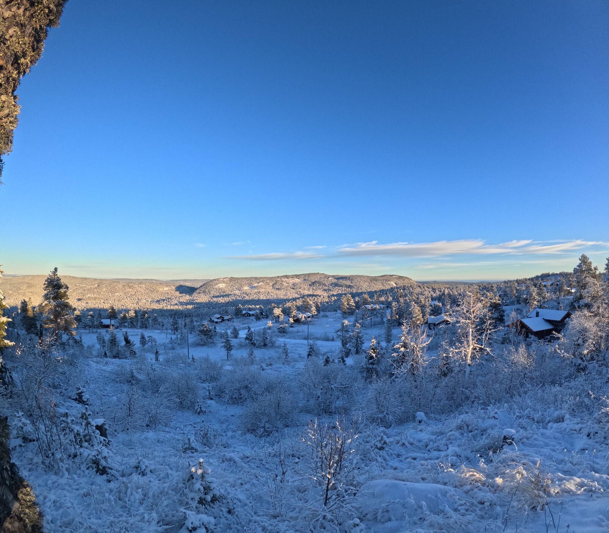 Paesaggio innevato con cielo sereno, alcune case e una catena montuosa in lontananza.