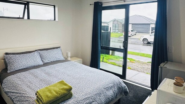 A hotel room with a bed, a small table with a kettle and cups, a window with curtains, and a view of the outside. - Room with En-suite and Kitchenette (Kaiapoi)