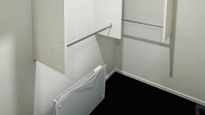A compact, white room with a built-in radiator, a metal shelf, and a blue cushion on the upper shelf. - Room with En-suite and Kitchenette (Kaiapoi)