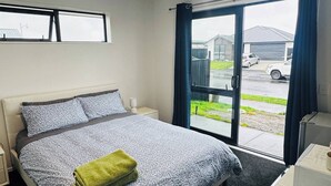 A hotel room with a bed, a desk with a coffee maker, and a view of the outside through a glass door. - Room with En-suite and Kitchenette (Kaiapoi)