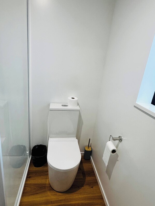 Un bagno piccolo e bianco con un water, un cestino nero e un porta carta igienica a parete.