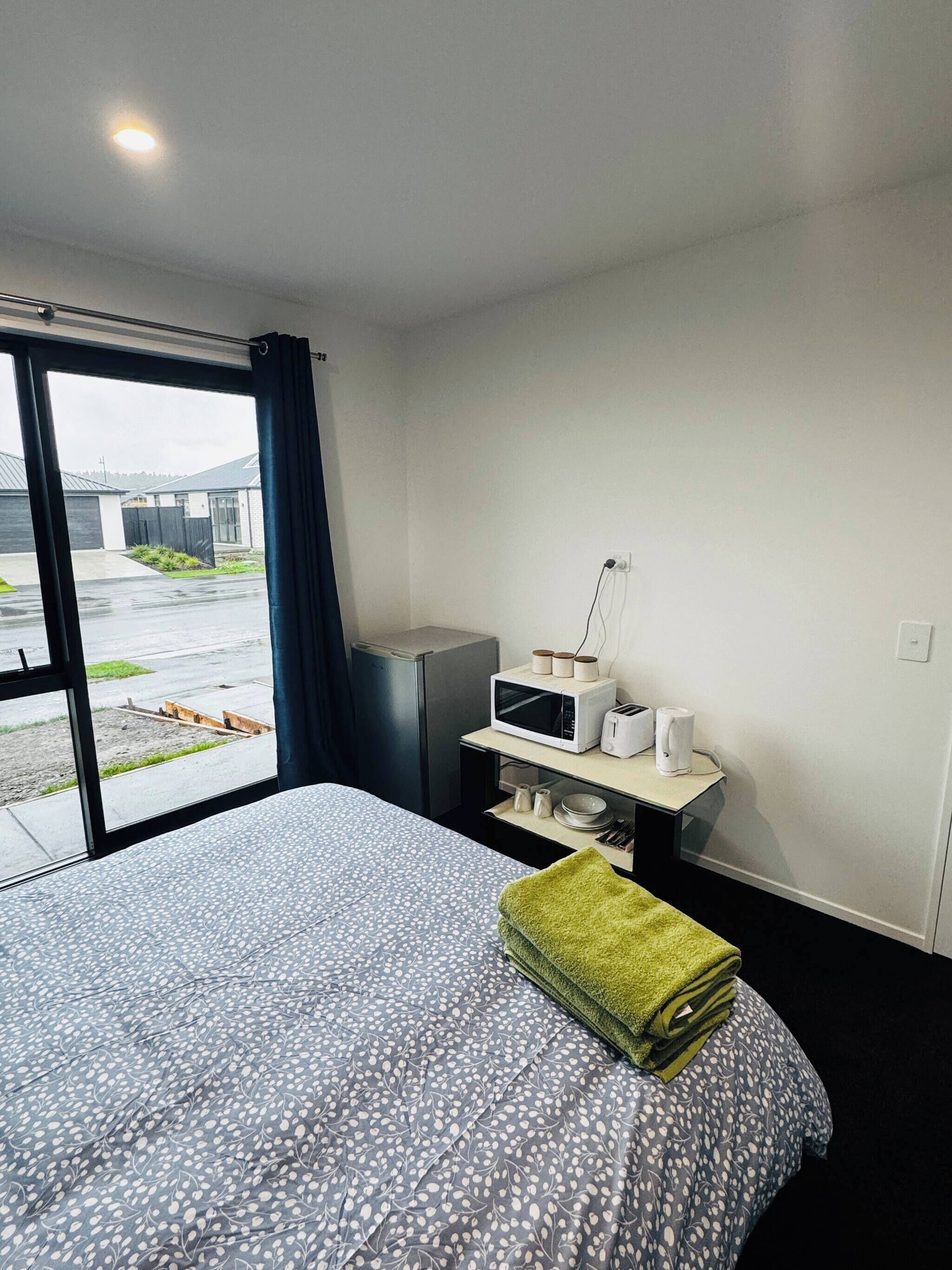 Une chambre d’hôtel avec un lit, une petite kitchenette, une fenêtre donnant sur l’extérieur et une porte.