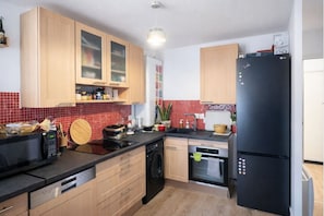 Una cocina compacta con armarios de madera, un refrigerador negro, un microondas y un lavavajillas.