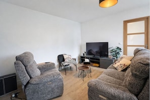 Una sala de estar moderna con dos sofás grises, una pequeña mesa de centro, un televisor sobre un estante negro y una puerta de madera.