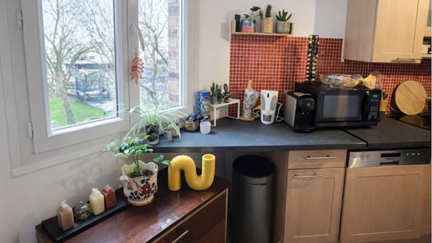 Una cocina con ventana, microondas, fregadero y varios utensilios sobre la encimera.