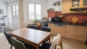 Una cocina con una mesa de comedor, sillas, armarios de madera, microondas y un salpicadero con azulejos rojos.
