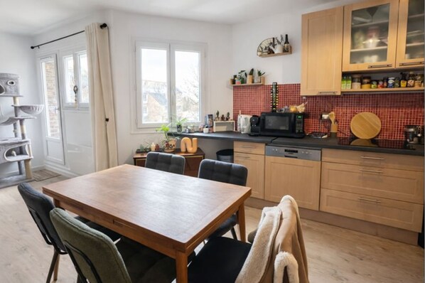 Una cocina con una mesa de comedor, sillas, armarios de madera, microondas y un salpicadero con azulejos rojos.