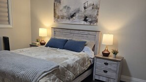 A bedroom with a large bed, two bedside tables with lamps, a nightstand, and a painting on the wall. - Comfortable City Home (Mississauga)