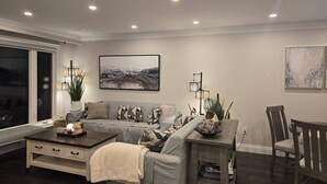 A modern living room with a sofa, coffee table, and a dining area with a chair. - Comfortable City Home (Mississauga)