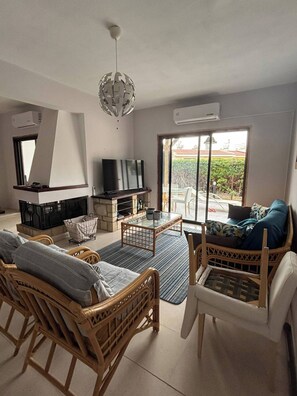 A living room with wicker furniture, a television, and a fireplace. - The Tala Townhouse Pafos (Tala)