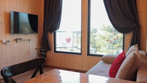 A room with a wooden interior, a flat-screen TV mounted on the wall, a sofa with cushions, a table, and a chair. - Delightful 1-bedroom villa with mountain view in Almaty (Besqaynar)