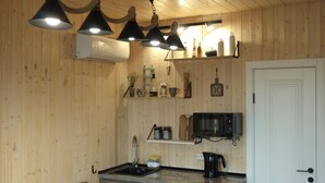 A compact kitchen with wooden walls, a white door, a microwave, a sink, and a coffee maker. - Delightful 1-bedroom villa with mountain view in Almaty (Besqaynar)
