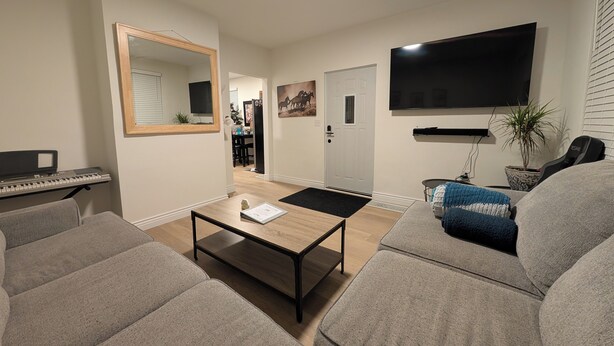 A living room with a sofa, a coffee table, a keyboard, a TV, and a door leading to another room.