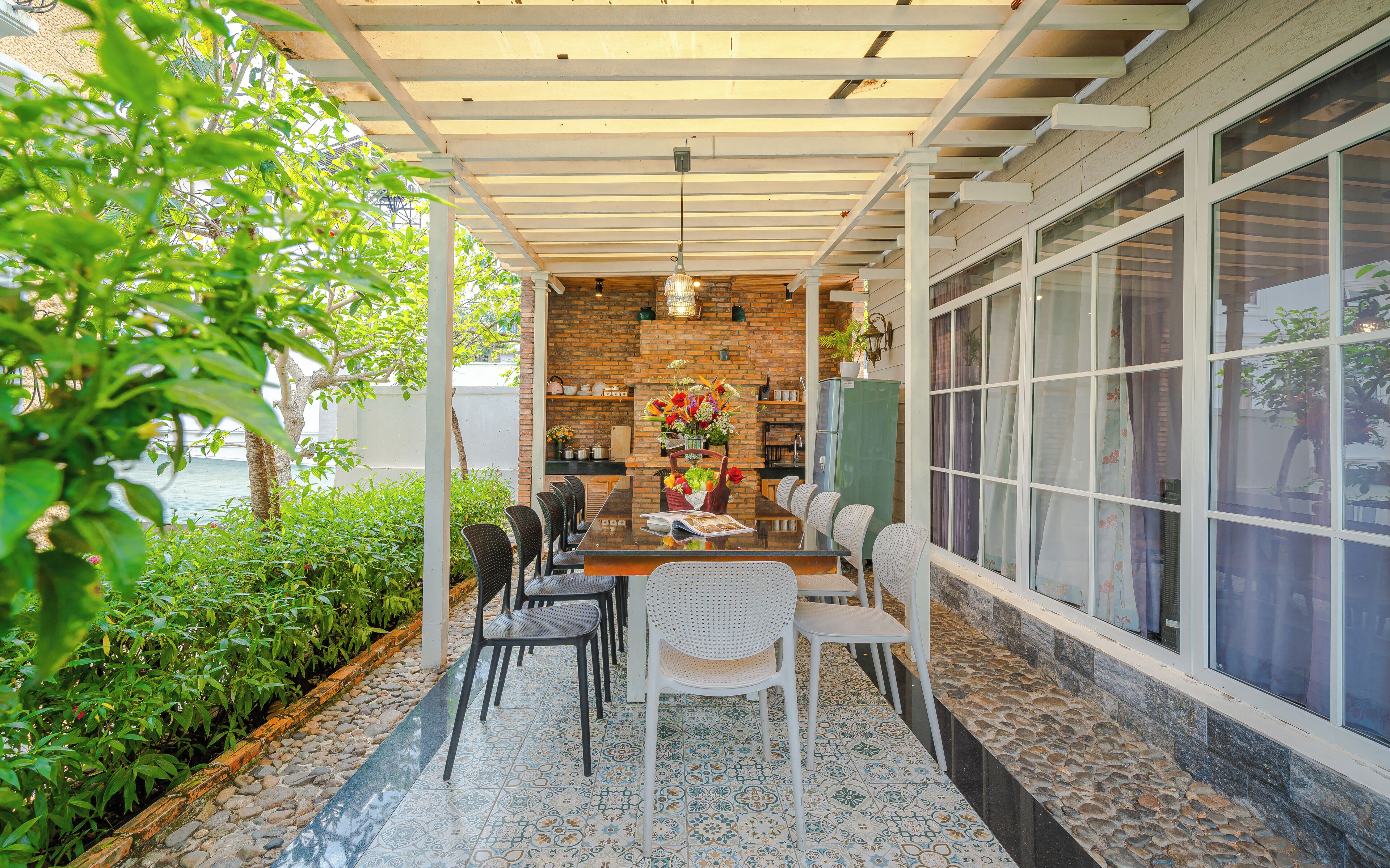 An outdoor patio with a brick wall, a dining table with chairs, and a large window.