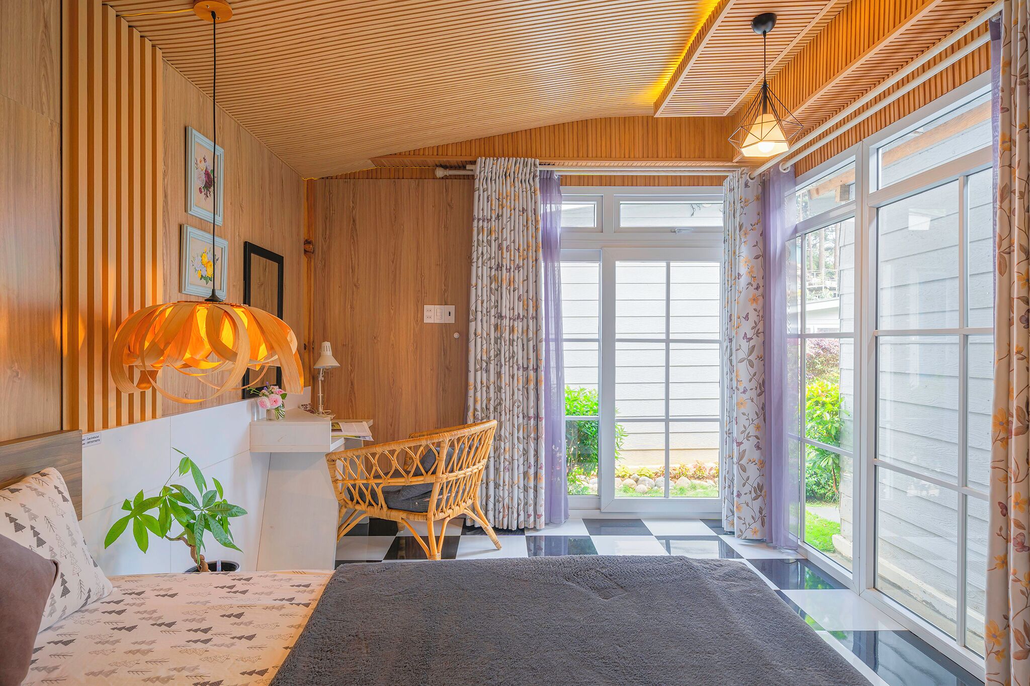 Una habitación acogedora con una cama, un escritorio y una silla. Hay un ventanal con cortinas, una planta y una lámpara.
