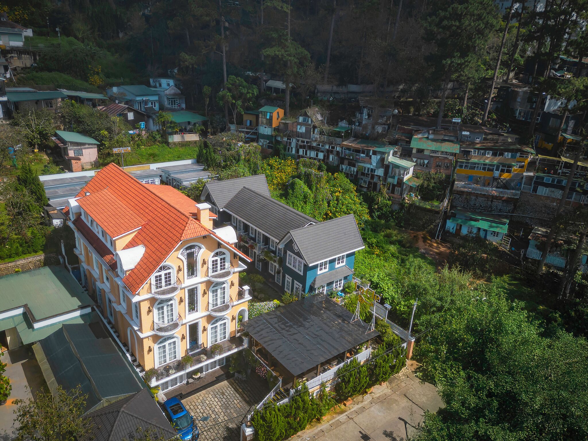 An aerial view of a residential area with multiple houses, including a prominent yellow house with a red roof and a blue house with a grey roof.