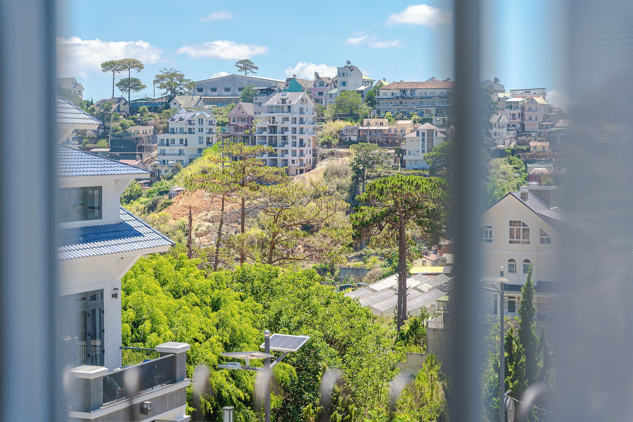 Un quartier résidentiel avec des maisons construites sur une colline, un balcon équipé d’un panneau solaire et un ciel dégagé.