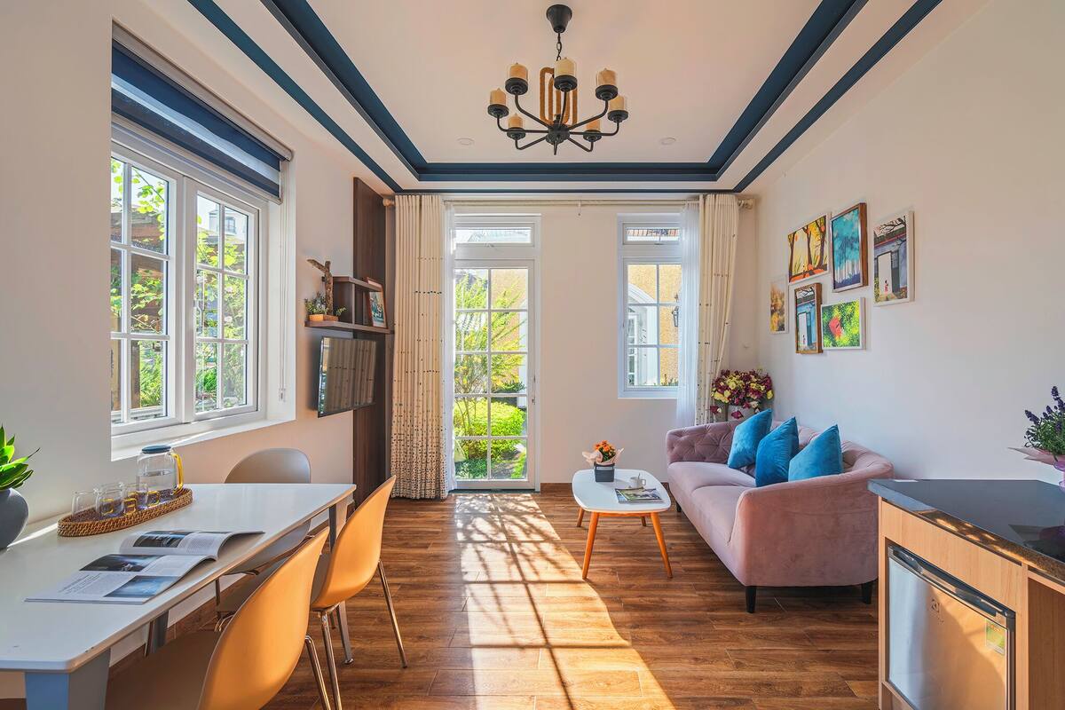 A well-lit room with a dining table, chairs, a sofa, and a kitchen area.