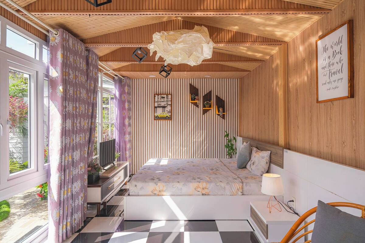 A bedroom with a bed, bedside table, lamp, and a view of the outdoors.