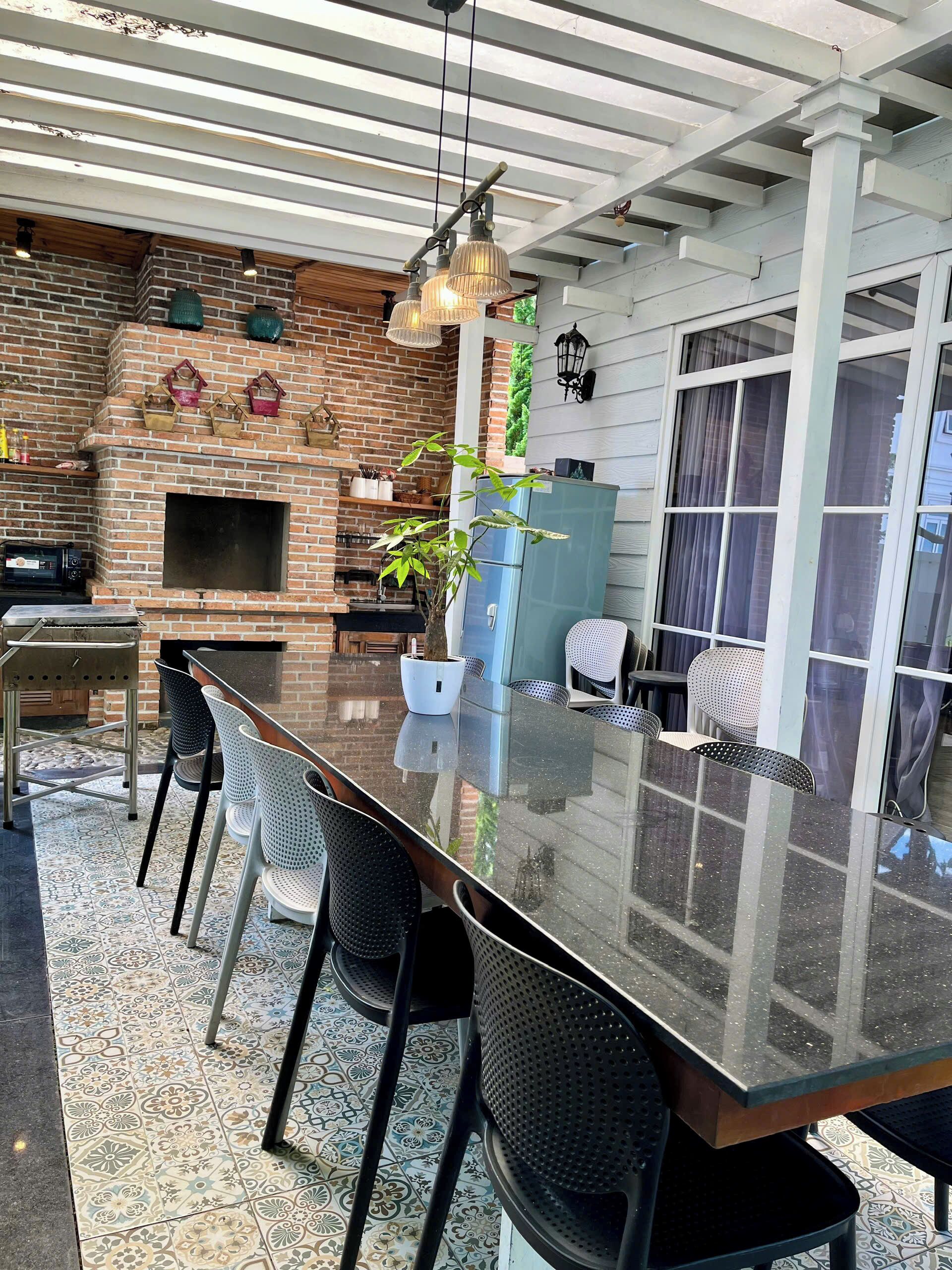 A covered outdoor dining area with a brick wall, a built-in grill, and a long table with chairs.
