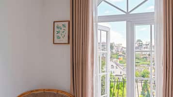 Una habitación con un amplio ventanal arqueado, una silla de mimbre, una mesita con un libro e impresión botánica enmarcada en la pared.